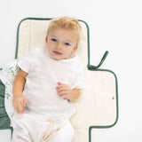 Baby lying on toddlekind baby portable changing clutch mini maven forest opened flat for diaper changing.