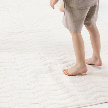 Close-up of child standing barefoot on padded mat texture – toddlekind portable water resistant wander grande play mat tofu for soft supportive flooring