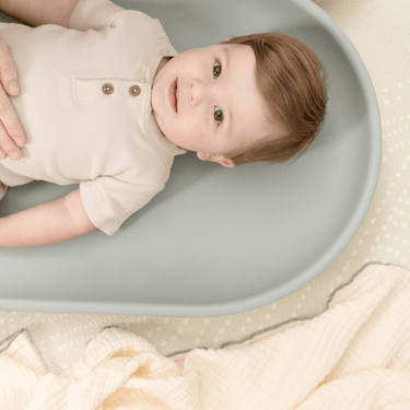 Baby resting comfortably on toddlekind baby foam changing pad nest pad sage with smooth cushioned surface.