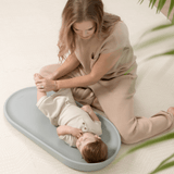 Parent adjusting baby on toddlekind baby foam changing pad nest pad sage in a calm nursery setting.