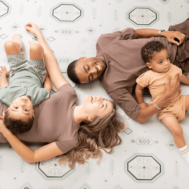 Parents and baby toddler lying on the mat smiling together, showcasing the toddlekind baby toddler foam modern designer puzzle play mat haven amira seagrass.