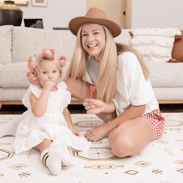 Parent and baby toddler sitting together smiling with lollipops on the toddlekind baby toddler foam modern designer puzzle play mat haven amira golden clay.