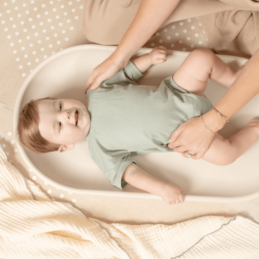 Baby lying comfortably on toddlekind baby foam changing pad nest pad turtle dove during diaper change.