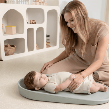 Smiling parent interacting with baby on toddlekind baby foam changing pad nest pad sage with ergonomic design.