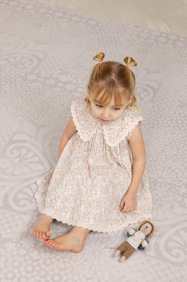 Young girl in a floral dress sitting on the haven playmat with a teddy bear.