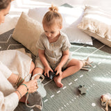 Toddler sitting on toddlekind baby toddler foam modern designer puzzle play mat haven berber moss playing with toys beside an adult and soft cushions.