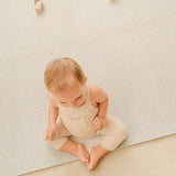 Baby sitting on the toddlekind baby toddler foam modern designer puzzle play mat haven deco ecru wearing neutral knit outfit.