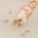 Baby lying on back playing with wooden blocks on toddlekind baby toddler foam modern designer puzzle play mat haven deco ecru.