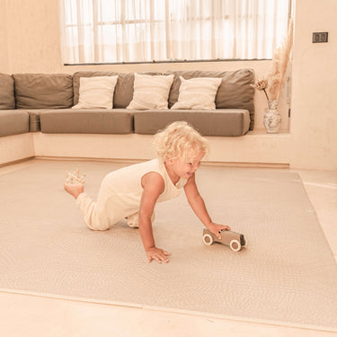 Toddler crawling and playing with a toy car on the toddlekind baby toddler foam modern designer puzzle play mat haven deco latte.
