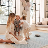 Mother sitting while toddler kisses baby on the cheek on the toddlekind baby toddler foam modern designer puzzle play mat haven linear mineral.