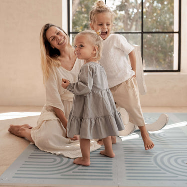 Smiling mother with baby and toddler playing together on the toddlekind baby toddler foam modern designer puzzle play mat haven linear mineral.