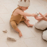 Baby reaching to hand a wooden block to an adult while sitting on the toddlekind baby toddler foam modern designer puzzle play mat haven tulum bone.