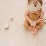 Baby wearing a soft crown sitting and playing with wooden blocks on the toddlekind baby toddler foam modern designer puzzle play mat haven tulum bone.