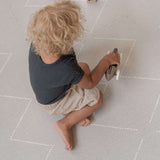 Toddler sitting and playing with a wooden toy car on the toddlekind baby toddler foam modern designer puzzle play mat haven tulum stone.