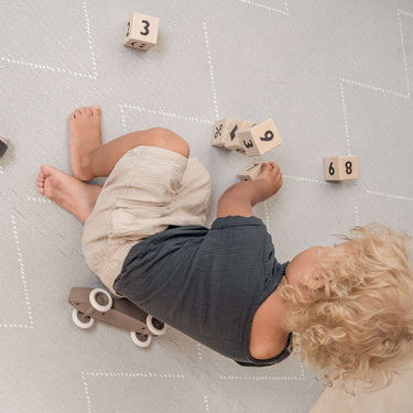 Toddler lying and playing with wooden number blocks on the toddlekind baby toddler foam modern designer puzzle play mat haven tulum stone.