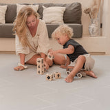 Mother and toddler playing with stacking blocks on the toddlekind baby toddler foam modern designer puzzle play mat haven tulum stone in a modern living room.