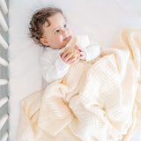 Baby lying comfortably with toddlekind 3 layer cotton muslin baby blanket kind cloth blush draped gently over body.