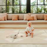 Baby sitting and laughing on toddlekind baby toddler foam modern designer puzzle play mat haven kyte mocha with soft toys nearby.