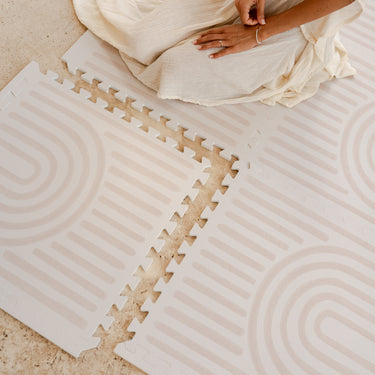 Overhead view of connected tiles with a person sitting on the floor demonstrating the toddlekind baby toddler foam modern designer puzzle play mat haven linear linen.