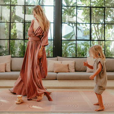 Mother dancing while toddler stands and plays on the toddlekind baby toddler foam modern designer puzzle play mat haven linear camel.