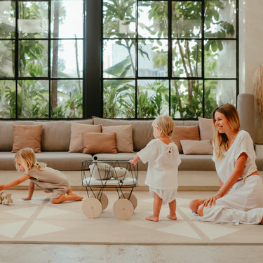 Two toddlers playing with toys while mother sits nearby on toddlekind baby toddler foam modern designer puzzle play mat haven kyte mocha in a modern home.