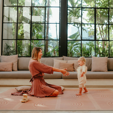 Mother reaching out as baby toddler walks toward her on the toddlekind baby toddler foam modern designer puzzle play mat haven linear camel.
