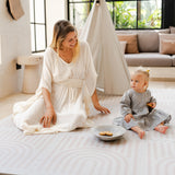 Mother and baby toddler sitting together indoors with cookies on the toddlekind baby toddler foam modern designer puzzle play mat haven linear linen.