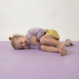 Toddler laughing while lying on side on toddlekind baby toddler foam modern puzzle play mat classic lilac.