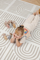 Child relaxing on the Toddlekind Linear Putty foam playmat with soft toys in a bright playroom.