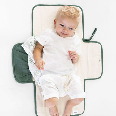 Baby resting on toddlekind baby portable changing clutch mini maven forest with side pockets and soft padding.