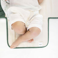 Close-up of baby legs on toddlekind baby portable changing clutch mini maven forest with soft cushioned interior.