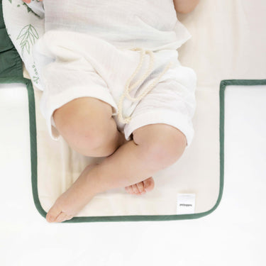 Close-up of baby legs on toddlekind baby portable changing clutch mini maven forest with soft cushioned interior.