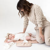 Parent changing baby on toddlekind baby portable changing clutch mini maven blush opened flat for easy diapering.