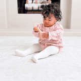 Toddler seated and examining a toy while sitting on the toddlekind baby toddler foam modern designer puzzle play mat haven parisa millet in a cozy living space.