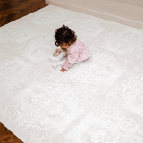 Overhead view of toddler sitting on a large assembled mat, highlighting full coverage of the toddlekind baby toddler foam modern designer puzzle play mat haven parisa millet.