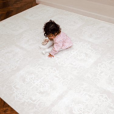 Overhead view of toddler sitting on a large assembled mat, highlighting full coverage of the toddlekind baby toddler foam modern designer puzzle play mat haven parisa millet.