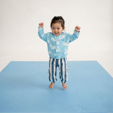 Smiling toddler standing with arms raised on toddlekind baby toddler foam modern puzzle play mat classic slate.