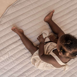 Overhead view of baby lying on organic cotton padded baby toddler toddlekind play mat tummy time quilted snuggle mat stone stripes with soft quilted lines.