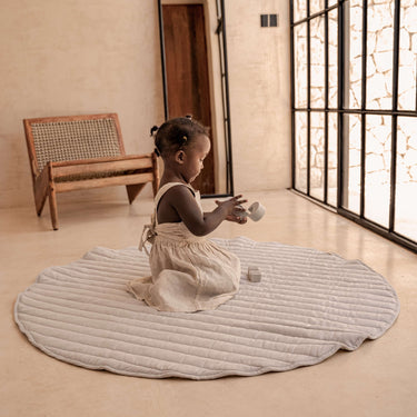 Toddler playing on organic cotton padded baby toddler toddlekind play mat tummy time quilted snuggle mat stone stripes in a bright minimal room.