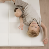 Baby lying on back smiling on toddlekind baby toddler foldable foam cushioned tumble play mat arden dove.