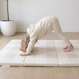 Toddler doing yoga pose on toddlekind baby toddler foldable foam cushioned tumble play mat arden dove in bright living space.