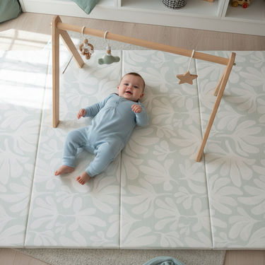 Baby lying under play gym on toddlekind baby toddler foldable foam cushioned tumble play mat willow frost.