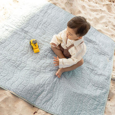 Toddler playing with a toy truck on a padded sage green mat in the sand, demonstrating the toddlekind portable water resistant wander classic play mat botanical sage for safe, comfortable play.