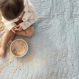 Overhead view of toddler playing with sand and a bowl on a sage green padded mat, illustrating the toddlekind portable water resistant wander classic play mat botanical sage for mess-friendly play.