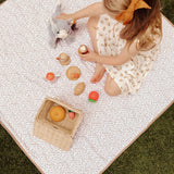 Child engaging in pretend play with toy food and a stuffed animal on a floral mat, featuring the toddlekind portable water resistant wander classic play mat botanical earthen for imaginative playtime.