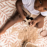 Overhead view of child holding sand and shovel while sitting on mat – toddlekind portable water resistant wander classic play mat ocean sea shell for sensory exploration