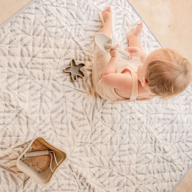 Overhead view of baby playing on soft leaf-pattern mat with bucket and scoop – toddlekind portable water resistant wander classic play mat ocean stone for easy cleanup