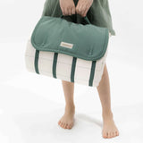 Child holding folded striped play mat with green flap and handle – toddlekind portable water resistant wander grande play mat forest for easy carrying