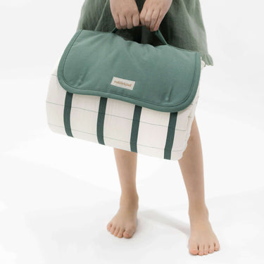 Child holding folded striped play mat with green flap and handle – toddlekind portable water resistant wander grande play mat forest for easy carrying