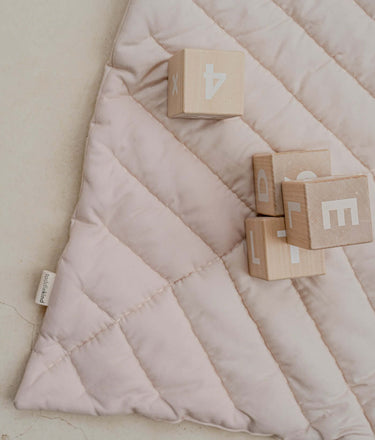 Close-up of organic cotton padded baby toddler play mat tummy time toddlekind quilted leaf mat blush with wooden blocks on stitched surface.